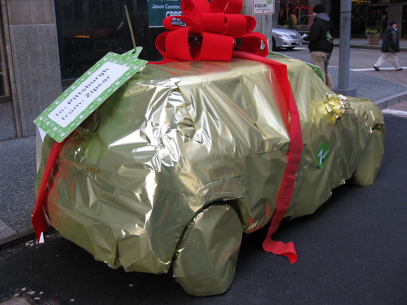 a color photo of a car wrapped in gold paper with a gigantic red bow